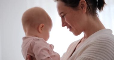 Yavru kızını kucaklayan ve gün ışığında kafasının tepesini öpen bir annenin yavaş çekimde yakın çekimi..