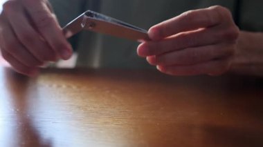 Yetişkin bir kadının masanda tırnak makasıyla tırnaklarını keserken görüntüsü. Minimalist manikür aletleri..