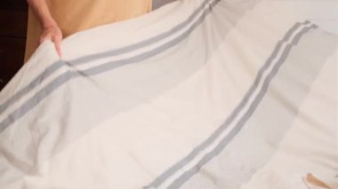 Yetişkin bir kadının yatak odasında yatak düzenlerken battaniye serdiği ve yatak düzenlerken yüzü görünmeyen yakın plan görüntüsü..