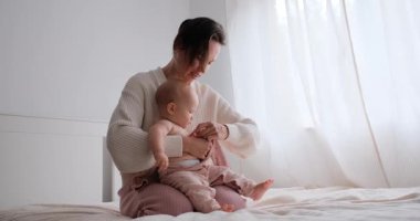 Bir anne bebeğini kucağında tutar ve oynar, gülümser ve birlikte yatakta alkışlar..