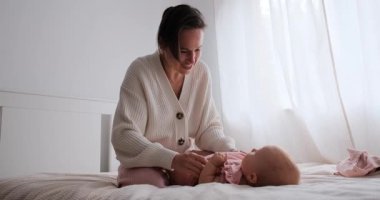 Bir anne bebeğini yatağa yatırır ve şakacı bir şekilde ayak parmaklarını öper..