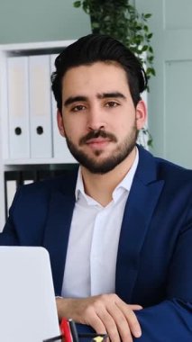 Yetişkin adam modern bir ofis ortamında dizüstü bilgisayar ve belgelerle yumuşak doğal ışık altında çalışır. Yavaş çekimde yakalanır..