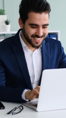 Yetişkin adam modern bir ofis ortamında dizüstü bilgisayar ve belgelerle yumuşak doğal ışık altında çalışır. Yavaş çekimde yakalanır..