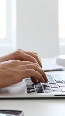 Yetişkin adam modern bir ofis ortamında dizüstü bilgisayar ve belgelerle yumuşak doğal ışık altında çalışır. Yavaş çekimde yakalanır..