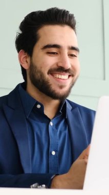 Yetişkin adam modern bir ofis ortamında dizüstü bilgisayar ve belgelerle yumuşak doğal ışık altında çalışır. Yavaş çekimde yakalanır..