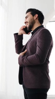 Yetişkin adam modern bir ofis ortamında dizüstü bilgisayar ve belgelerle yumuşak doğal ışık altında çalışır. Yavaş çekimde yakalanır..