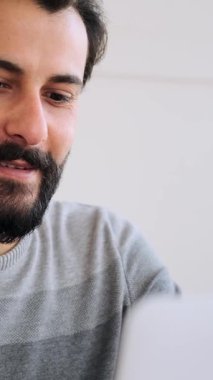 Parlak bir ofiste dizüstü bilgisayarla çalışırken gülümseyen yetişkin bir adamın yakın çekimi..