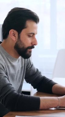 Bilgisayarda yazan yetişkin bir adamın yan görüntüsü, basılı bir belgeyi kontrol etmek ve parlak bir ofiste çalışmaya devam etmek..