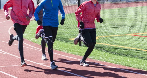 Four track and field athletes are running together on a red track during winter track, wearing gloves and spandex.