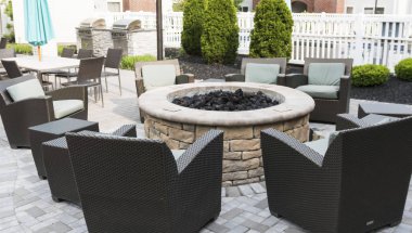 A hotels patio is set up with a fire pit and chairs with tables and umbrelllas and a barbeque grill for friends and families to relax, clipart