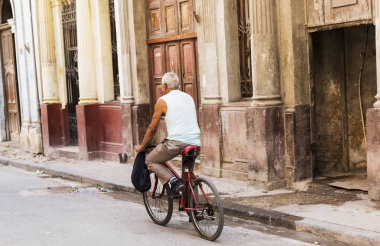 Havana Küba içinde belgili tanımlık geçmiş renkli binalar ile beatup yollarda adam onun bisiklet ile gidiyor.