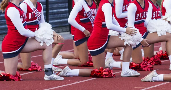 High school cheerleaders take a knee during another squads performance on the field.