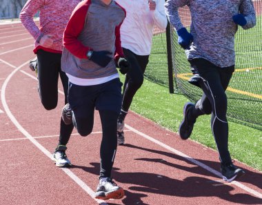 Bir grup dört koşucu çoğu eğitim birlikte yolda bir kırmızı kış eldiven ve uzun kollu gömlek giyiyor.