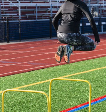 Bir kadın atletizm sprinter iki ayak ile tribünün arka planda yeşil çim sahada strenctgh, denge ve koordinasyon için sarı Engelli atlıyor, 