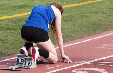 Bir lise kadın sprinter başlayan blok bir kırmızı rayına açık havada onun sprint yarışı başlatmaya hazır mevcuttur.