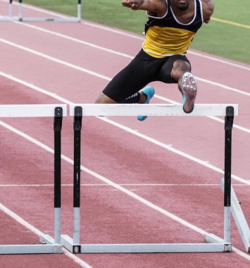 An African American high school track and field athlete racing over a hurdle. clipart