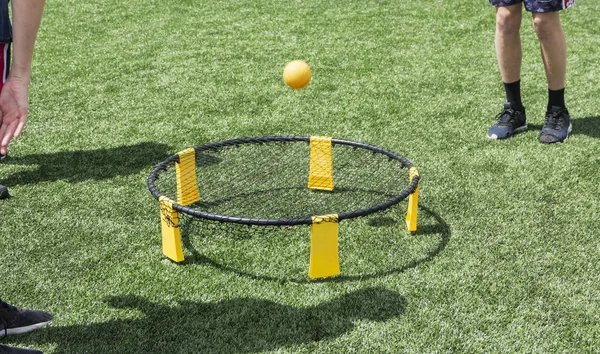 Teenagers playing spike ball with the ball bouncing off of the net on a green turf field.