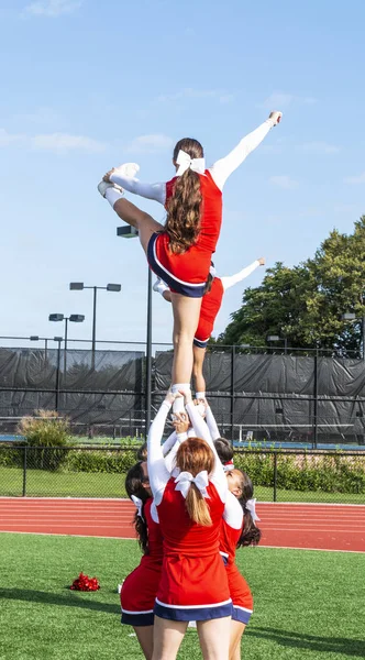 Cheerleaders in a pyramid practicing holding their teammate up by thieir ankles before homecoming.