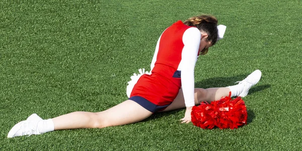 A high school cheerleader is in a split on a green turf field weaing a red, white and blue outfit.