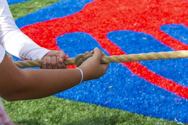 Hands gripping the knot in the rope during a tug of war game on a turf field.