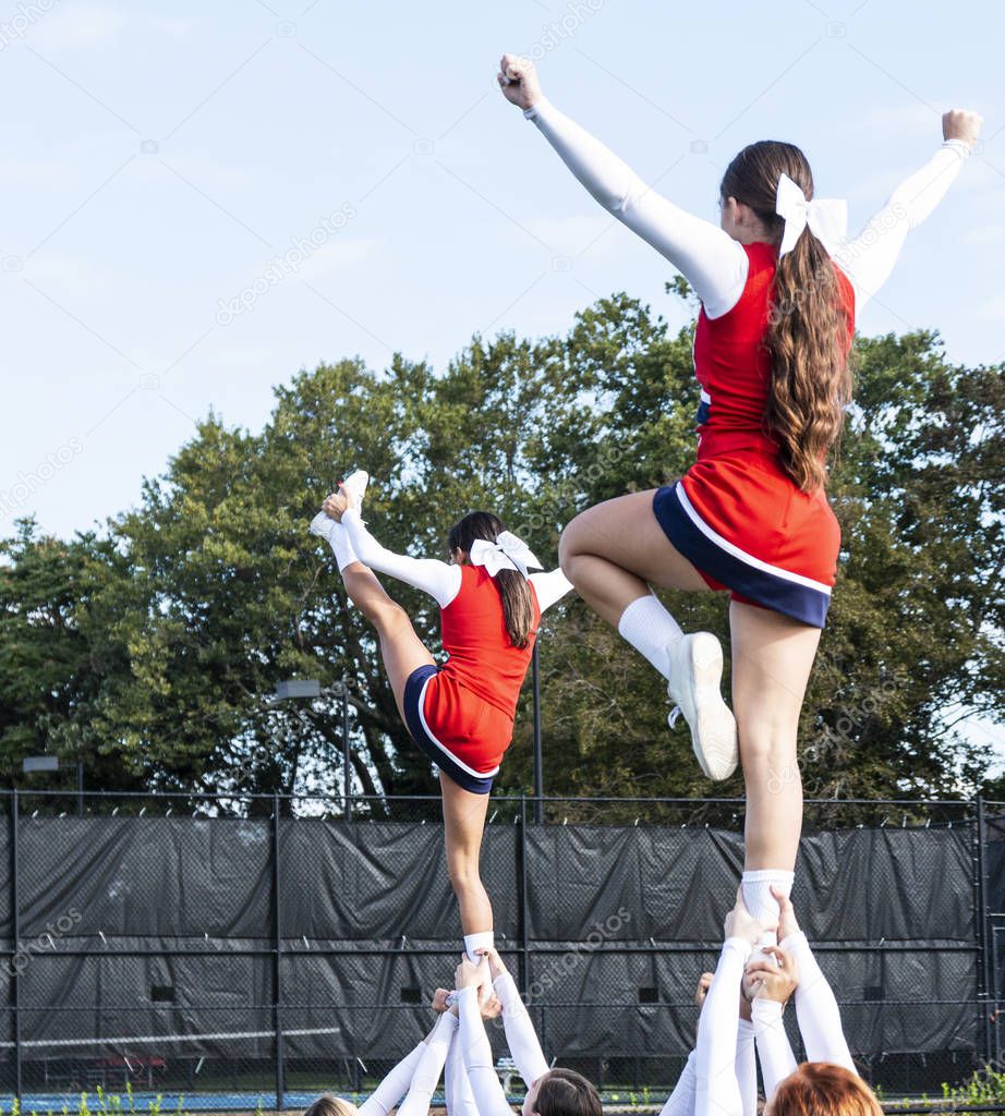 Two high school cheerleading squads holding up their teammates by their ankles while they still perform and cheer.