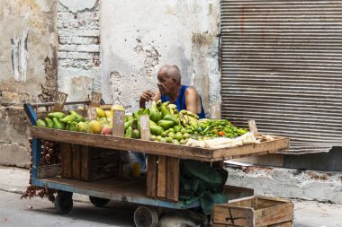 Havana, Küba'da - 25 Temmuz 2018: Havana Küba sokaklarında meyve satan bir sigara onun meyve sepeti arkasında oturan bir adam.