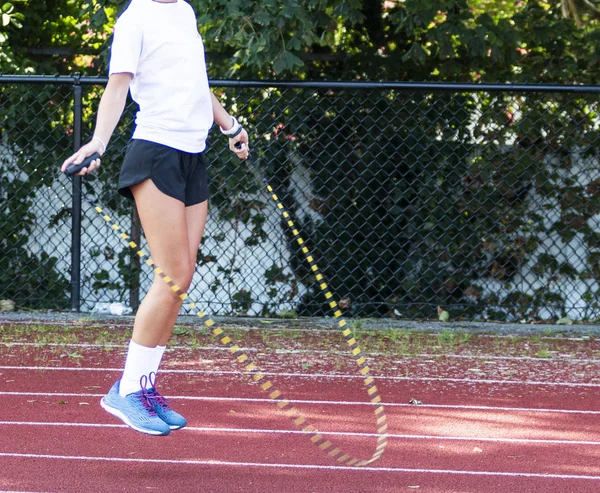 A female high school track and field athlete is jumping rope on a track.
