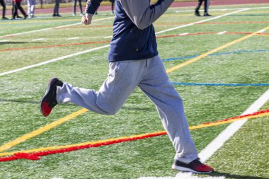 Bir lise sprinter kış atletizm antrenman sırasında yeşil çim sahada çalışıyor.