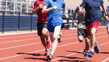 A group of high school boys are running together on a red track during practice in the summer.