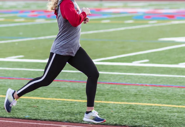 A female distance runner is training by running fast intervals on a track in spandex and long sleeves.