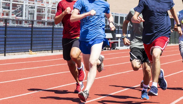 A group of high school boys are running together on a red track during practice in the summer.