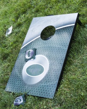 Bir yeşil metal Mısır delik oyun etrafında fasulye torbaları ile uzun boylu yeşil çimenlerin üzerinde yatıyor.