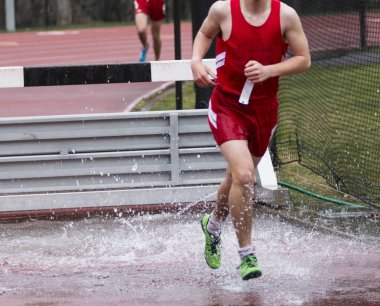 Bir lise çocuk 3000 metre hendekli olay bir yarış çalıştırırken su çukur çıkıyor.