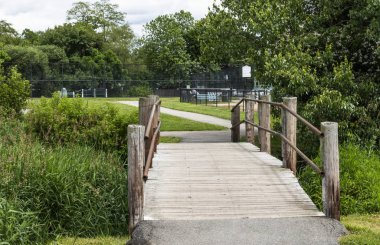 Uzun boylu yeşil ot ve çalılar tarafından çevrili bir ahşap köprü geçit bakarak ve doğrudan tenis kortlarında seyir görünümü.