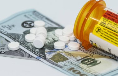 A pill bottle has its pills spilling out onto a couple of one hundred dollar bills. clipart