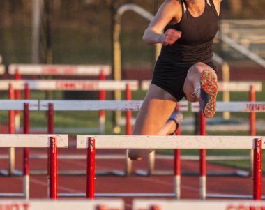 Female runner racing hurdles outdoors clipart