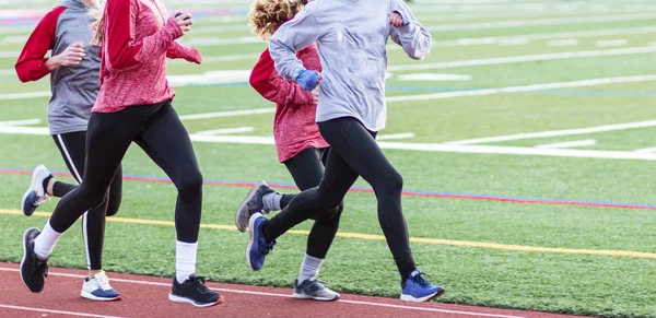 Quatro meninas do ensino médio correndo em uma pista — Fotografia de Stock