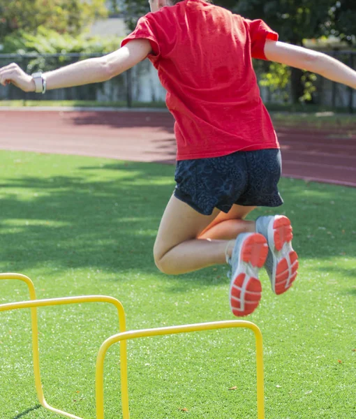 Female athlete jumping over two foot yellow hurdle — Stock Photo, Image