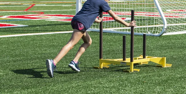 Atleta spingendo slitta gialla attraverso campo di tappeto erboso verde — Foto Stock