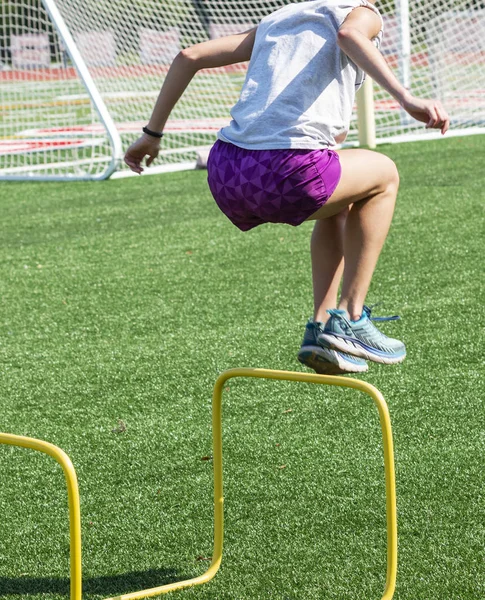 Teenager-Mädchen in lila Shorts springt über gelbe Hürden — Stockfoto