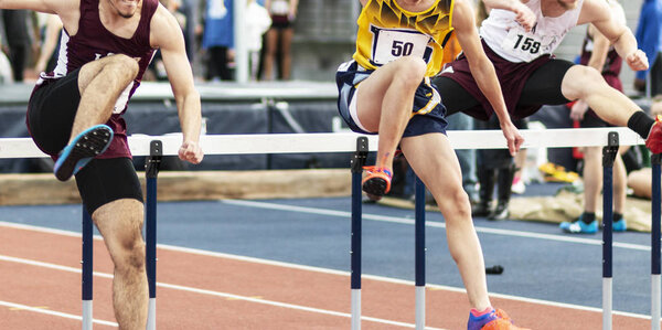 Three runners racing the hurdles indoors