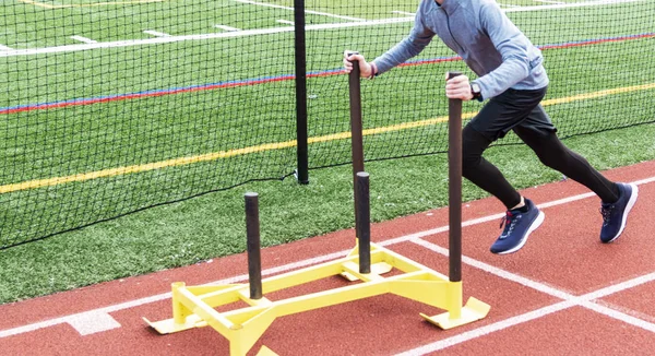 Jovem atleta empurrando trenó em uma pista — Fotografia de Stock