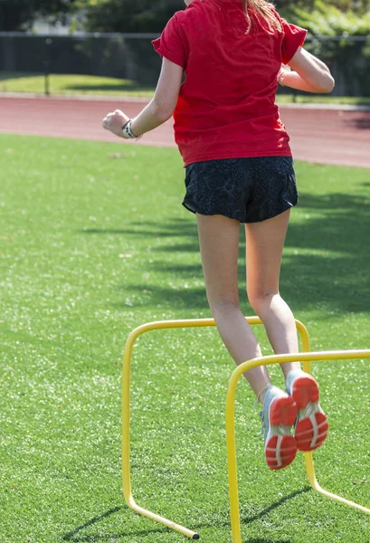Atleta feminina saltando sobre mini barreiras amarelas — Fotografia de Stock
