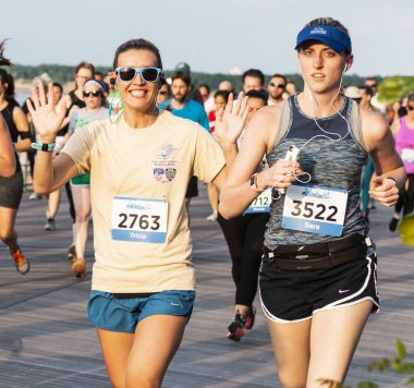 10 km 'lik koşu yarışında kadınlar el sallıyor ve gülümsüyor.