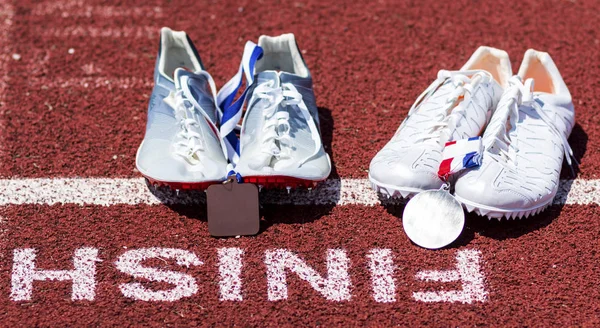 Runniners racing spikes at finish line with gold and siver medal