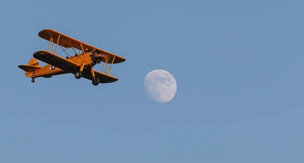 Antique biplane flying with full moon and blue sky