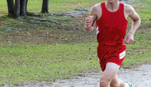 High school cross country runner in red uniform racing on a dirt