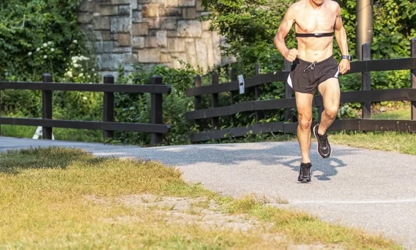 Corredor sem camisa usando monitor de frequência cardíaca em trilha no parque — Fotografia de Stock