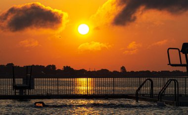 Havuzda yüzücü wate üzerinde yükselen güneşi yansıtan