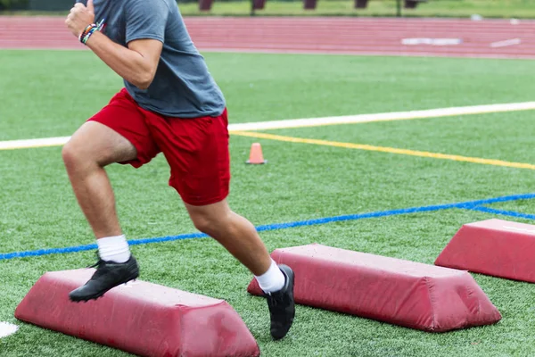 Спортсмен, бегущий по красным барьерам на поле в бутсах — стоковое фото